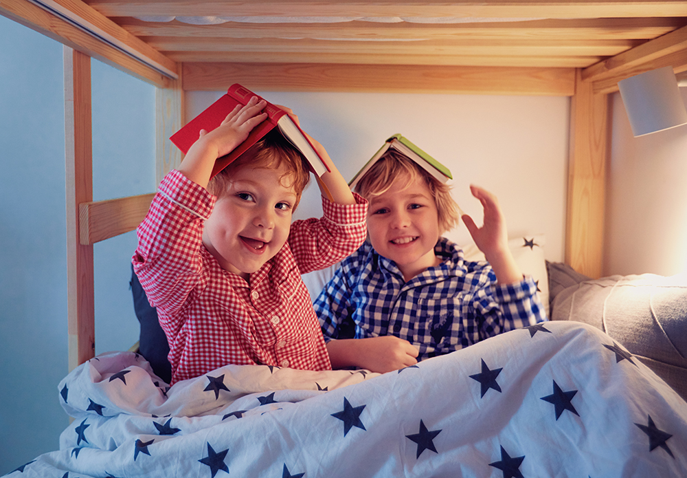 cheerful kids, brothers having fun, playing with books on the bunk bed during bedtime